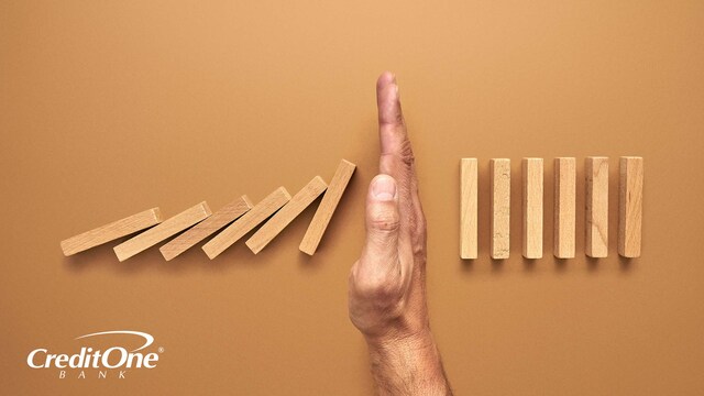 An extending hand reaches out to halt a series of falling dominoes, perhaps signifying how filing for Chapter 7 bankruptcy can halt ongoing debt and provide a fresh start.